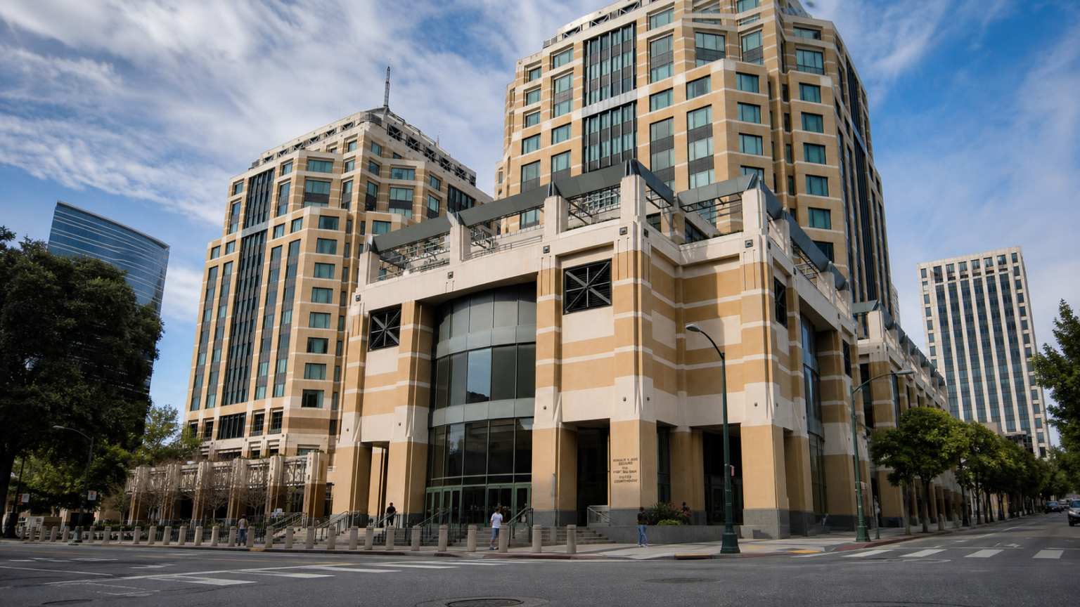 Pedestrians walk outside a large tan federal office and courthouse complex on a clear morning.