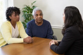 An older adult and younger adult in an office conversation with a third person, editorial illustration