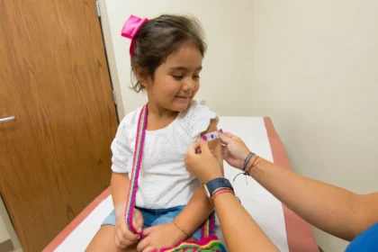 Editorial illustration of a child watching a healthcare worker place a bandage on her upper arm.
