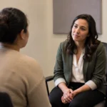 Two adults having a seated intake conversation in a modest community-service office.