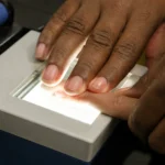 Editorial illustration of a technician guiding a finger onto an illuminated fingerprint scanner.