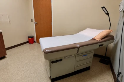 Editorial illustration of a padded examination table, pillow, and examination lamp in an ordinary outpatient room.