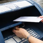 Editorial illustration of hands placing a stamped envelope into an open blue postal collection box.