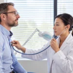 Clinician listening to a seated adult man’s chest with a stethoscope