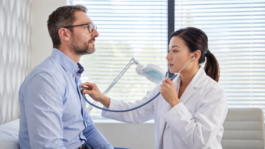 Clinician listening to a seated adult man’s chest with a stethoscope