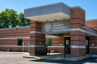 Editorial illustration of a brick community health center entrance with a canopy, bench, and accessible curb route