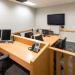 Editorial illustration of a small administrative hearing room with wood partitions, office chairs, and hearing equipment.